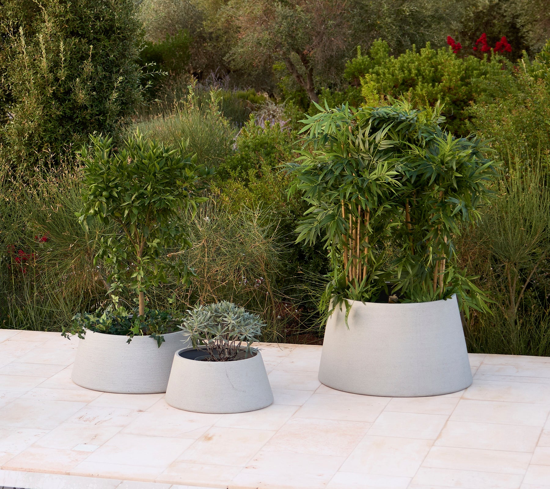 Tres macetas grises modernas con varias plantas en un entorno de jardín.