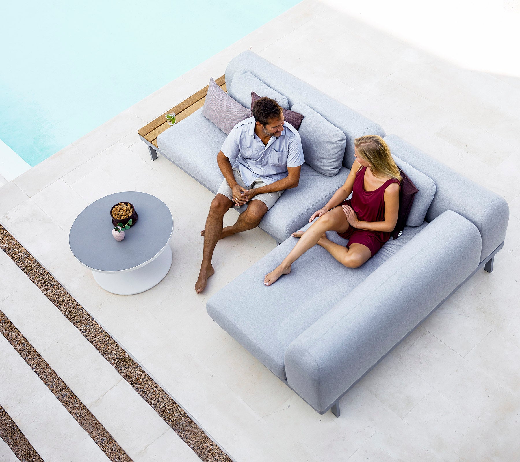 Un hombre y una mujer están sentados en un sofá gris moderno, involucrados en una conversación, con una mesa pequeña y artículos decorativos cerca.