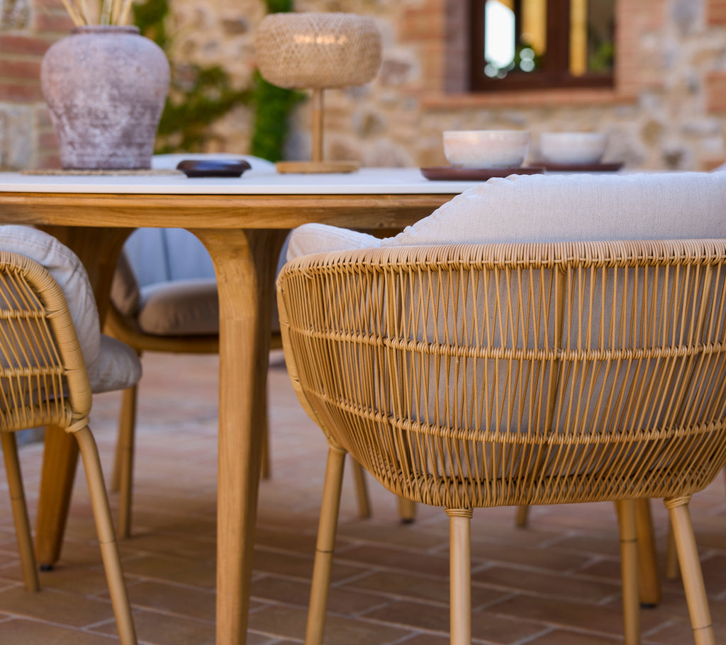 Entorno de comedor elegante con sillas tejidas con patas de aluminio alrededor de una mesa de madera moderna, complementado con elementos decorativos.