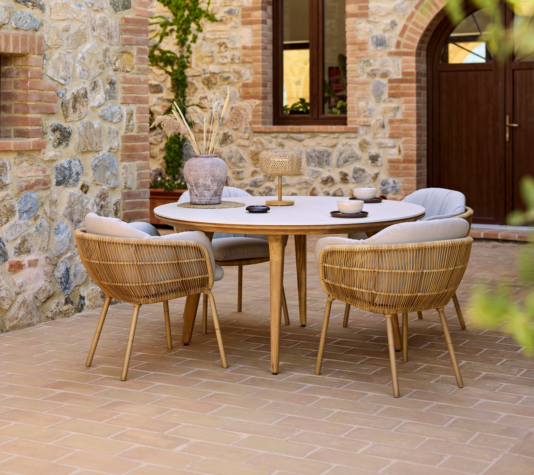 Montaje de comedor al aire libre con una mesa redonda Aspect y sillas Stay, con un fondo de pared de piedra.