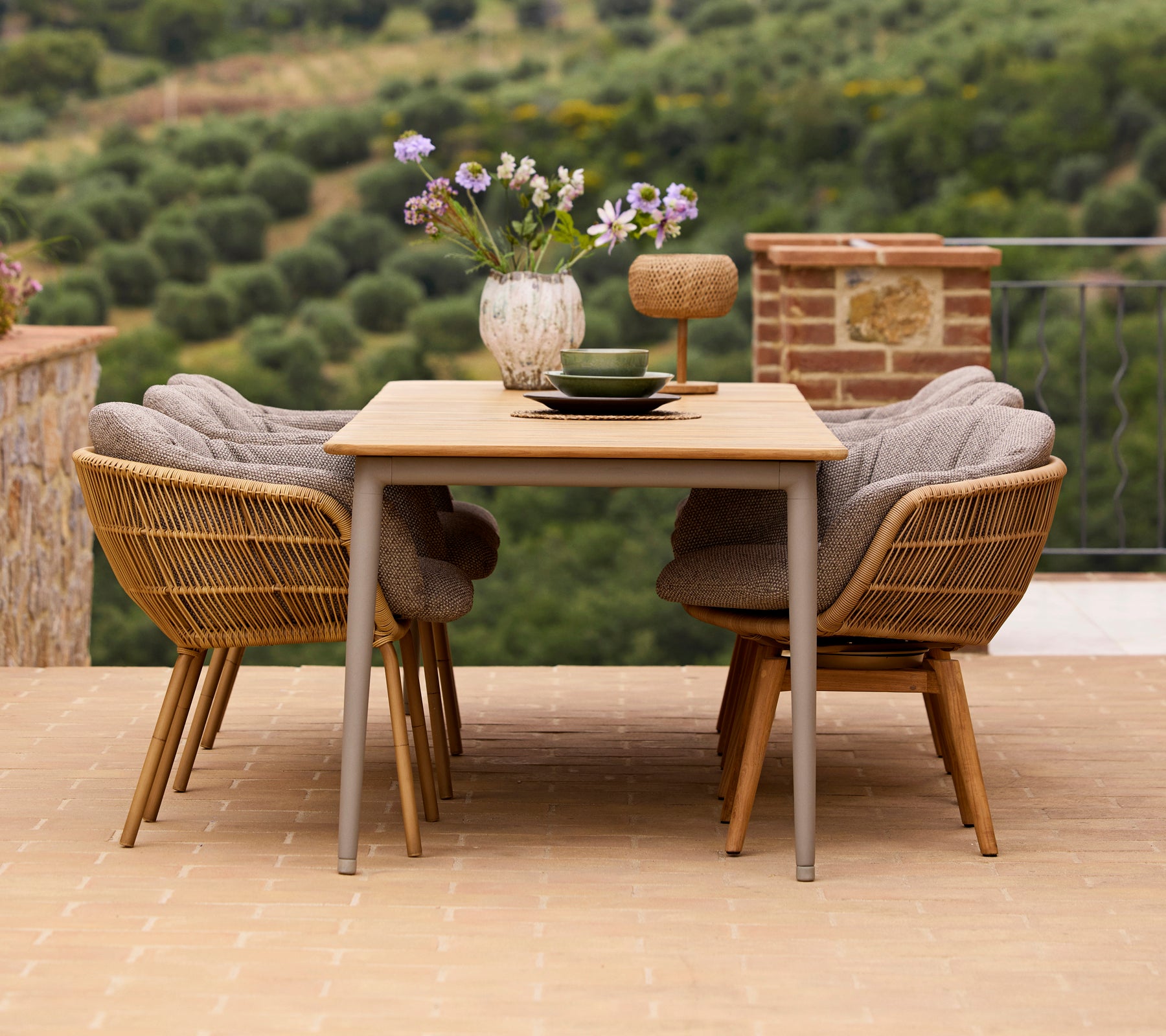 Conjunto de comedor elegante con una mesa de madera, dos sillas Stay con patas de aluminio y un jarrón de flores con accesorios decorativos.