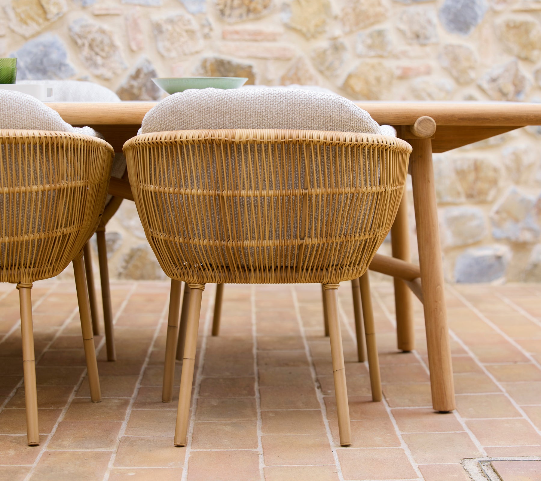 Dos sillas de comedor tejidas con patas de aluminio situadas junto a una mesa de comedor de madera, con una estética natural.