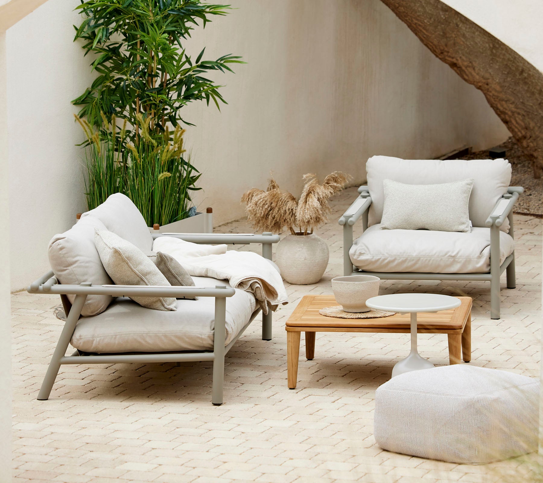 Arreglo de asientos acogedor con cojines suaves, una mesa de café de madera y elementos decorativos, rodeado de vegetación.