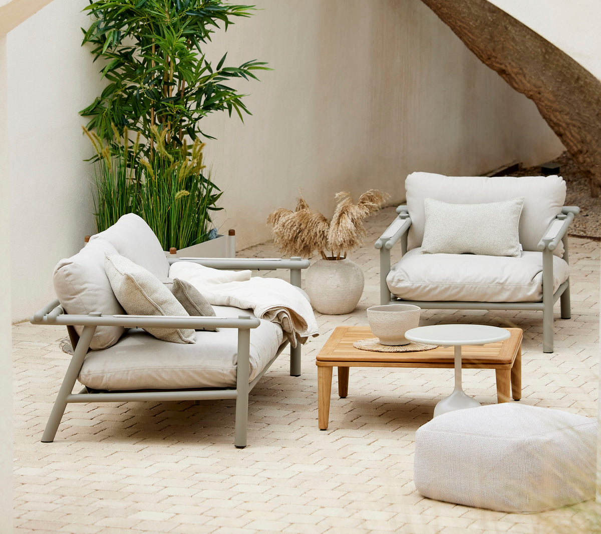 Arreglo de asientos acogedor con cojines suaves, una mesa de café de madera y elementos decorativos, rodeado de vegetación.