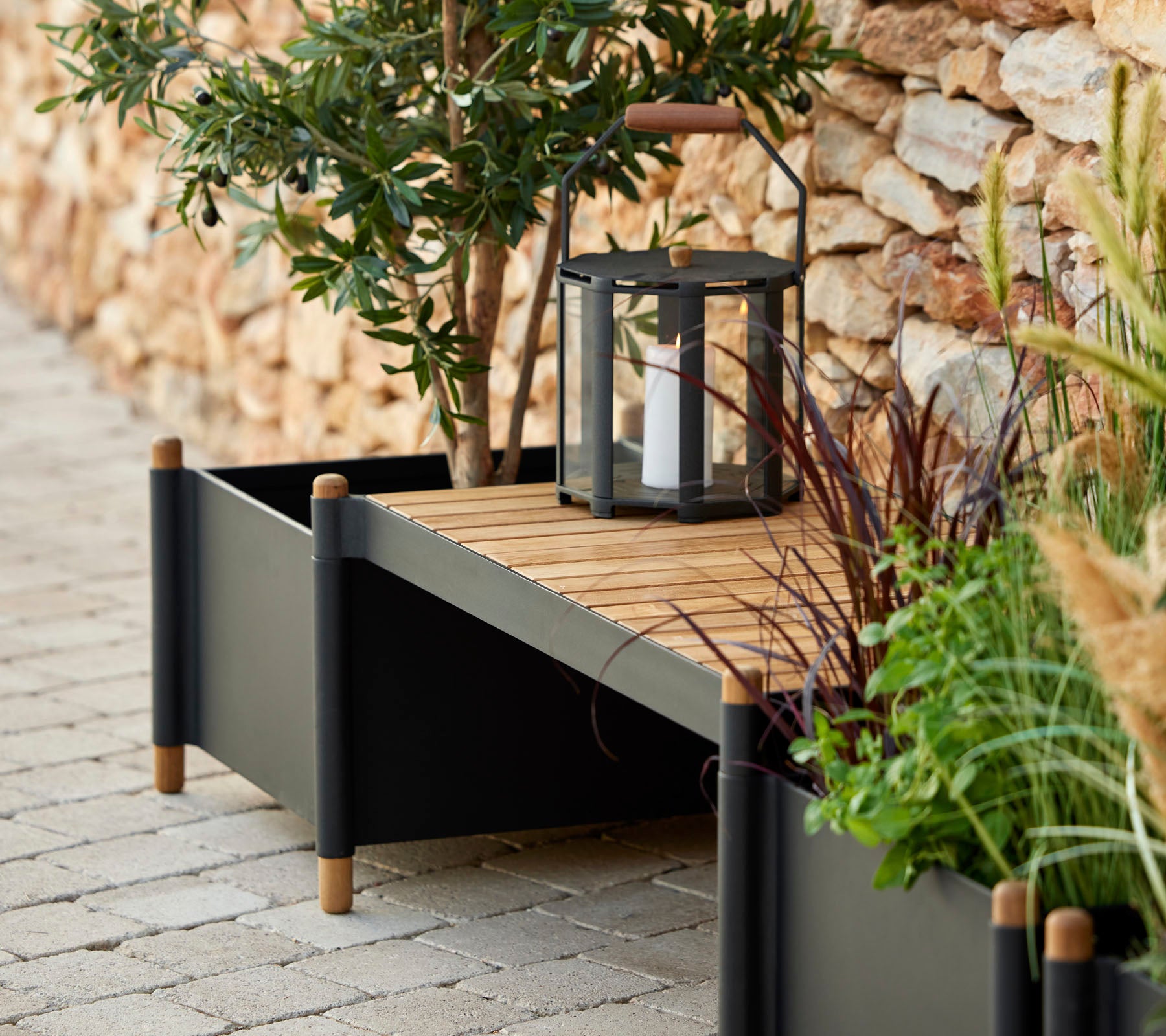 Una elegante caja de plantas con tablones de madera, rodeada de vegetación y una linterna, que aporta un toque de elegancia al espacio.