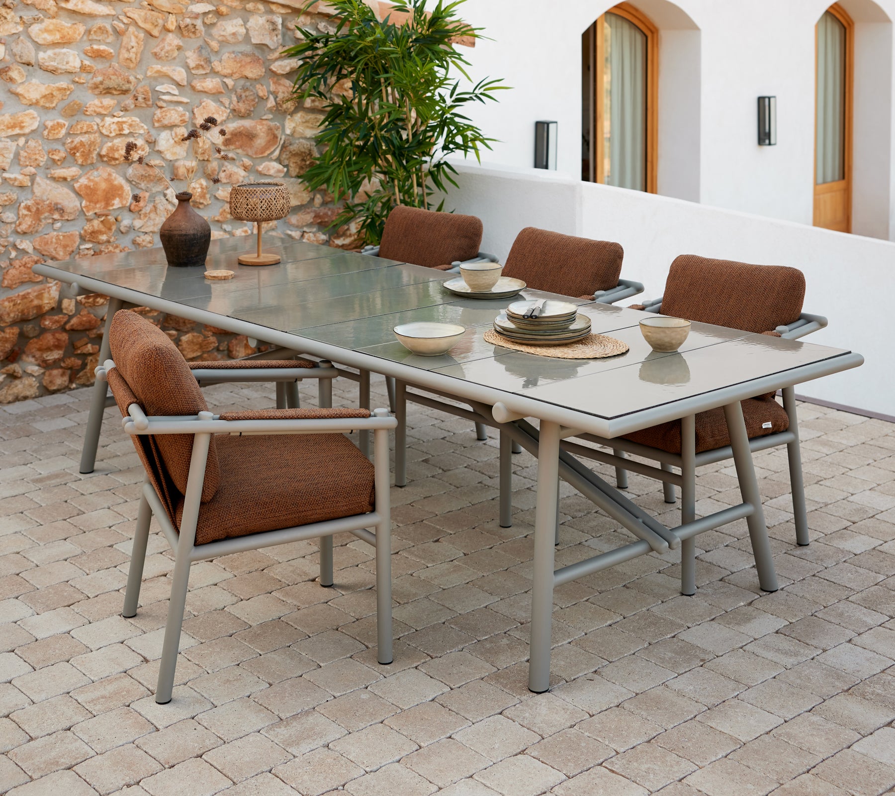 Un juego de mesa de comedor espacioso con varillas de aluminio, con sillas acolchadas marrones y cubiertos dispuestos sobre una superficie de vidrio.