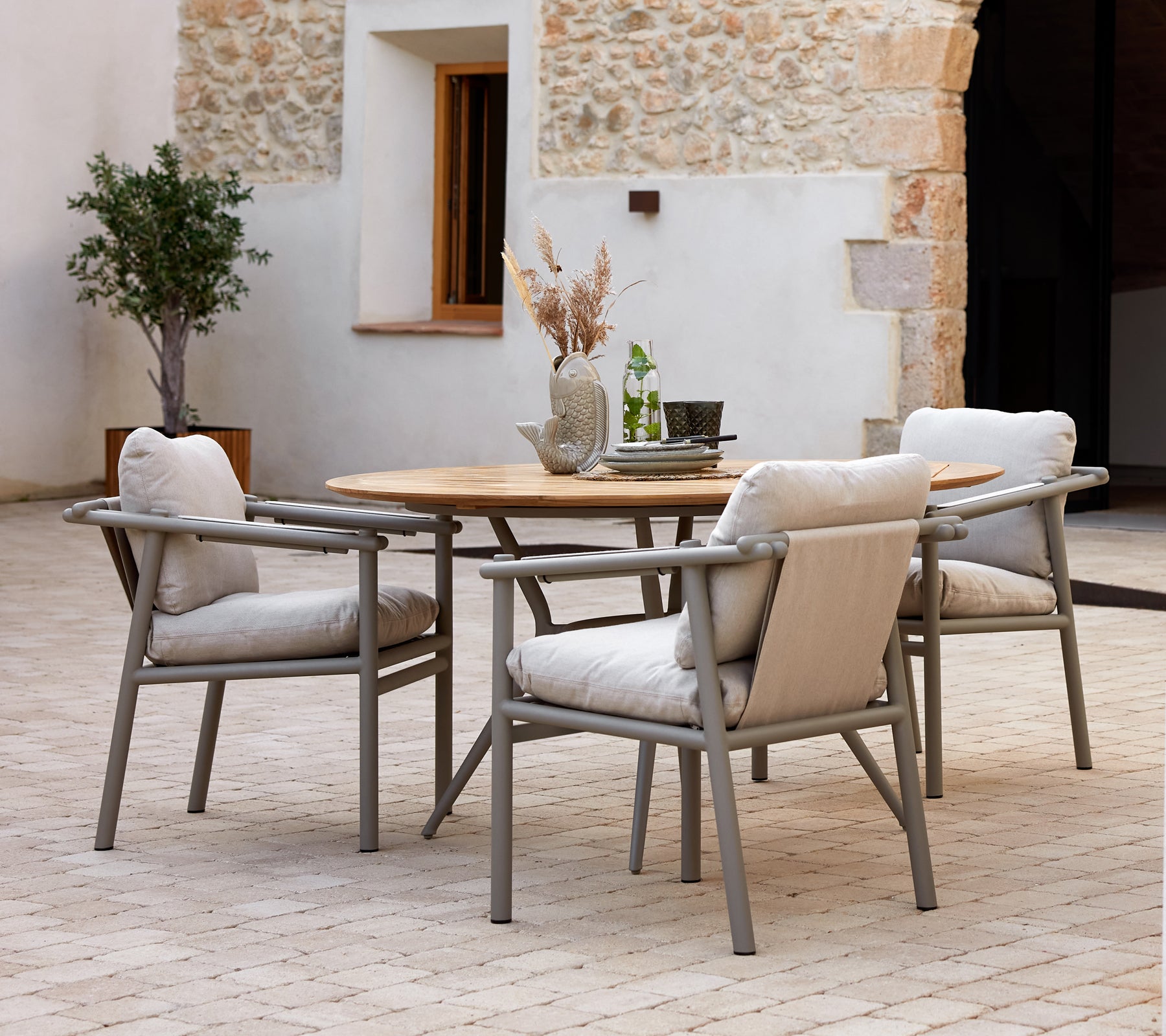 Mesa de comedor moderna con una superficie de madera y marcos de aluminio, acompañada de suaves sillas acolchadas, contra un fondo texturizado.