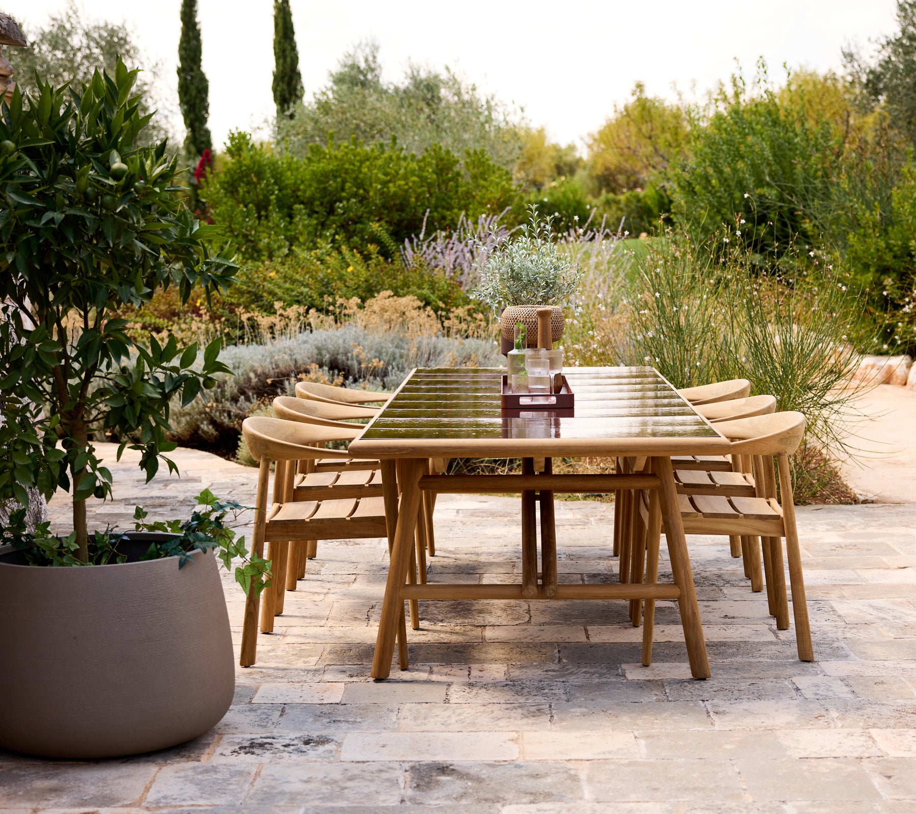 Mesa de comedor moderna al aire libre con sillas de madera en un entorno de jardín.