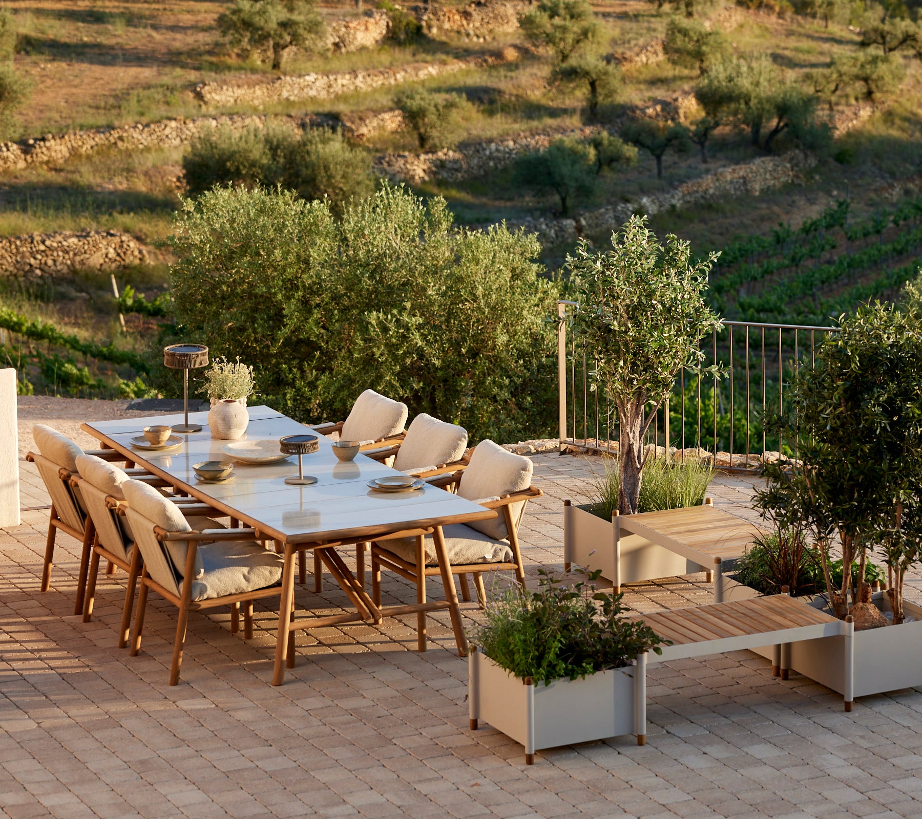 Un conjunto de comedor elegante con acentos de teca, que cuenta con sillas cómodas y un banco para plantas, rodeado de vegetación.