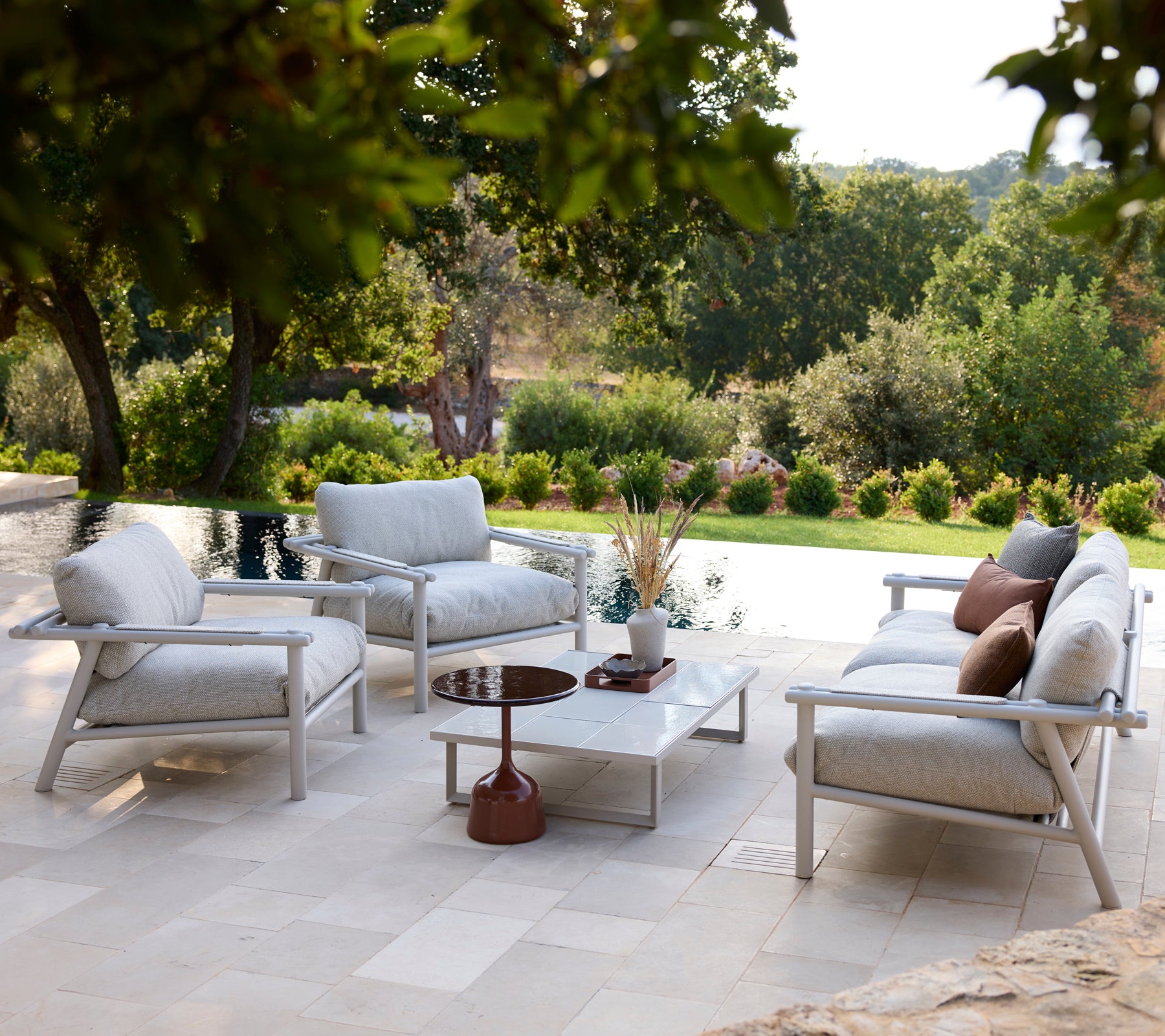 Área de lounge exterior moderna con sillas blancas, cojines grises y una mesa blanca.