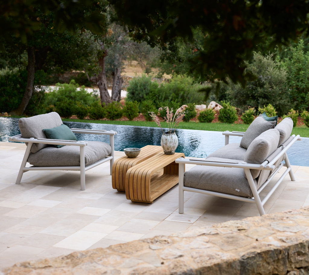 Área de lounge moderna con sillas blancas con cojines grises y una mesa de café de madera.