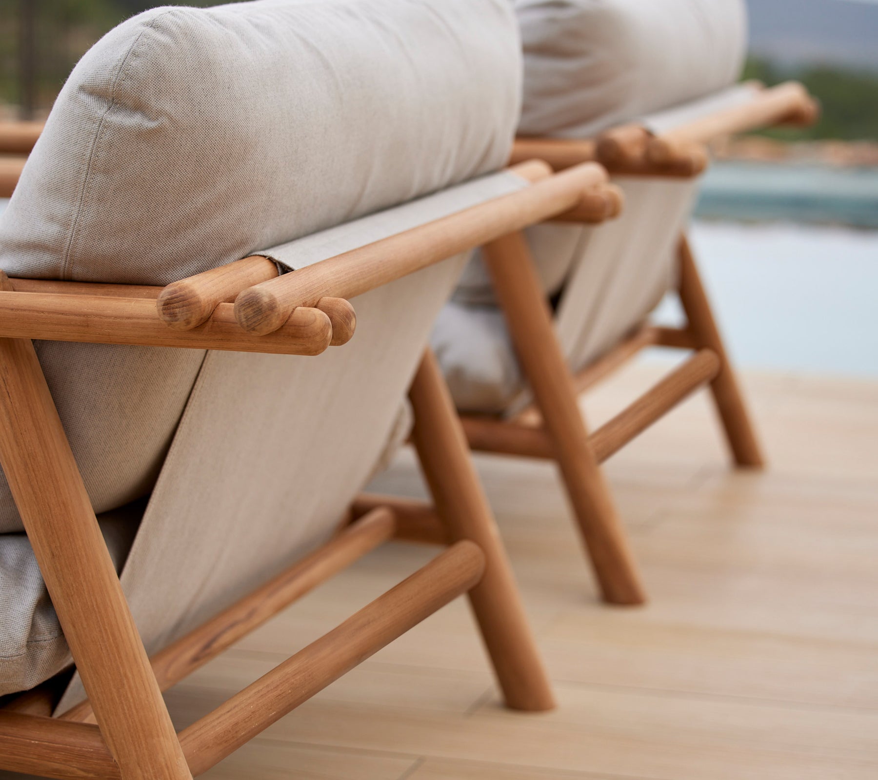 Dos sillones elegantes con marcos de teca y cómodos cojines beige, que presentan un diseño único de varilla en el respaldo.