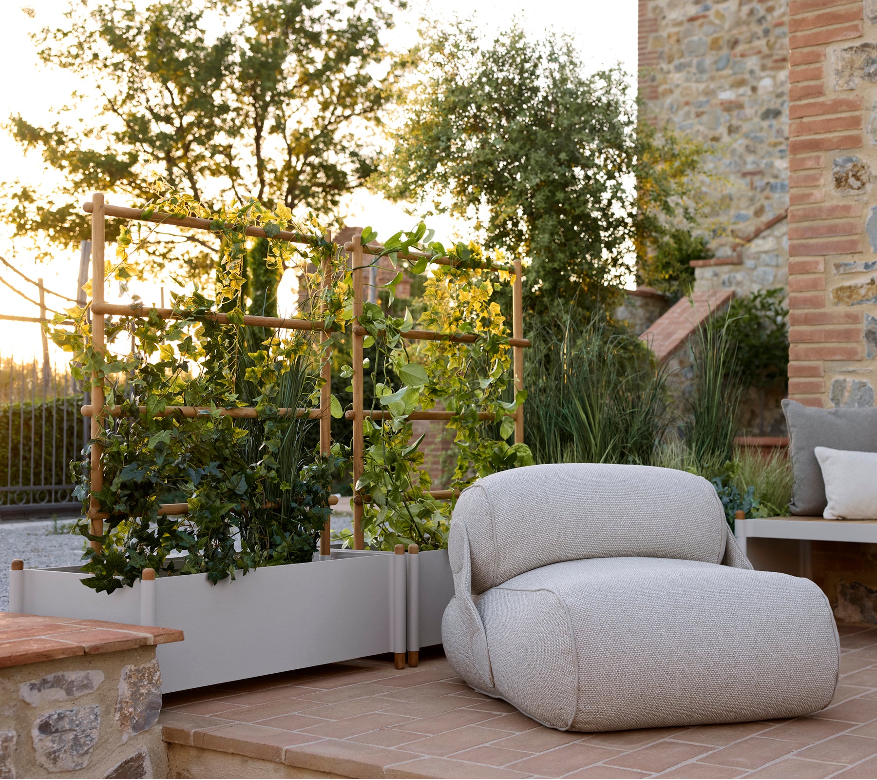 Sillón lounge suave al lado de una maceta elegante, con vegetación y un entorno exterior sereno con cálida luz natural.