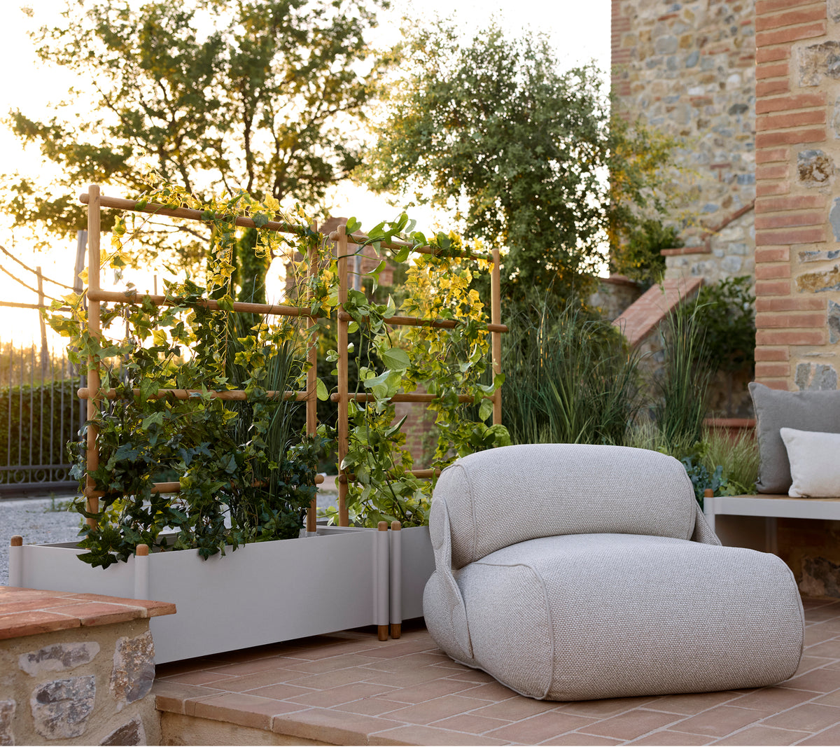 Sillón lounge suave al lado de una maceta elegante, con vegetación y un entorno exterior sereno con cálida luz natural.