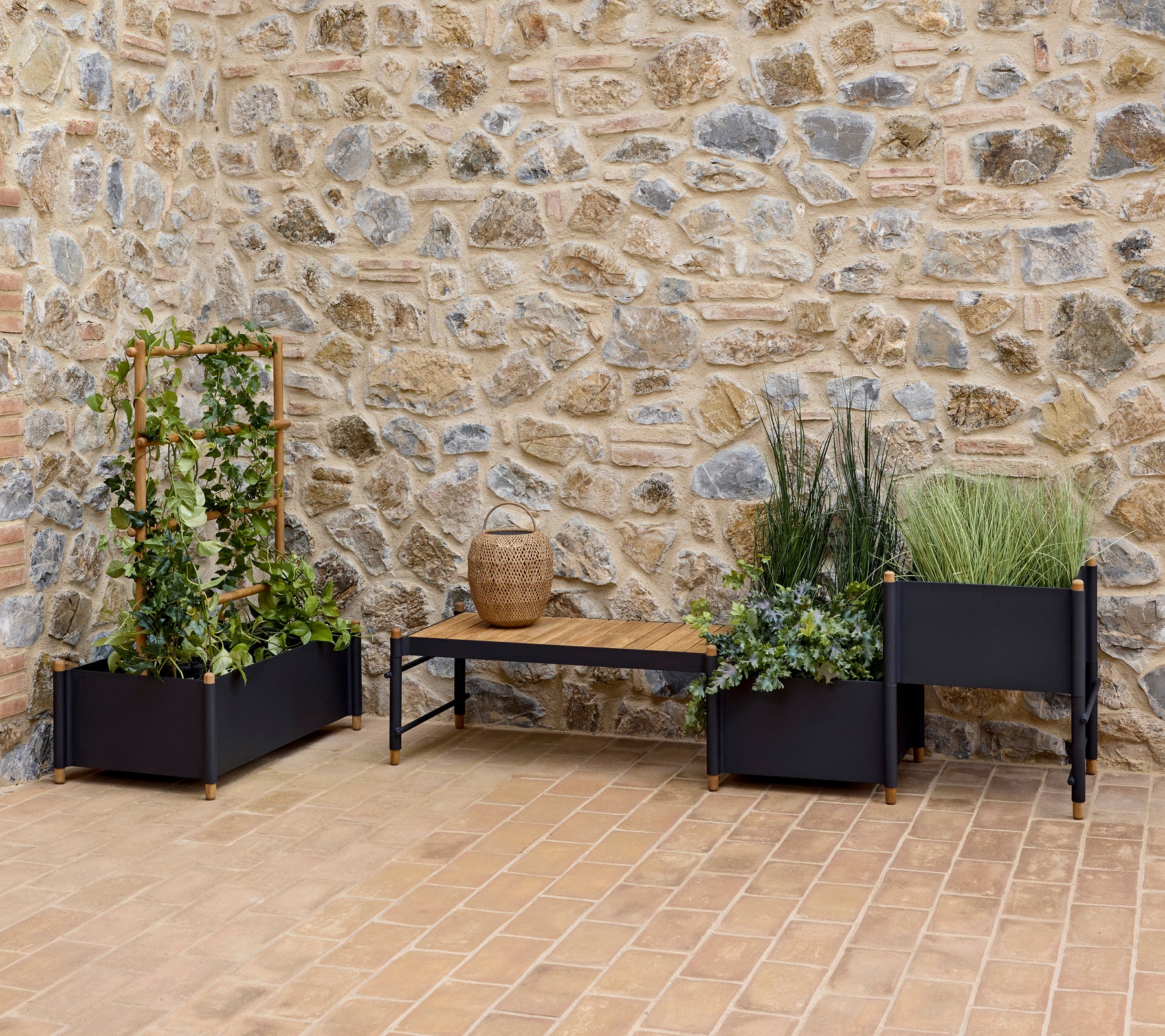 Macetas elegantes con abundante vegetación y un banco, frente a una pared de piedra texturizada, que realzan un espacio exterior sereno.