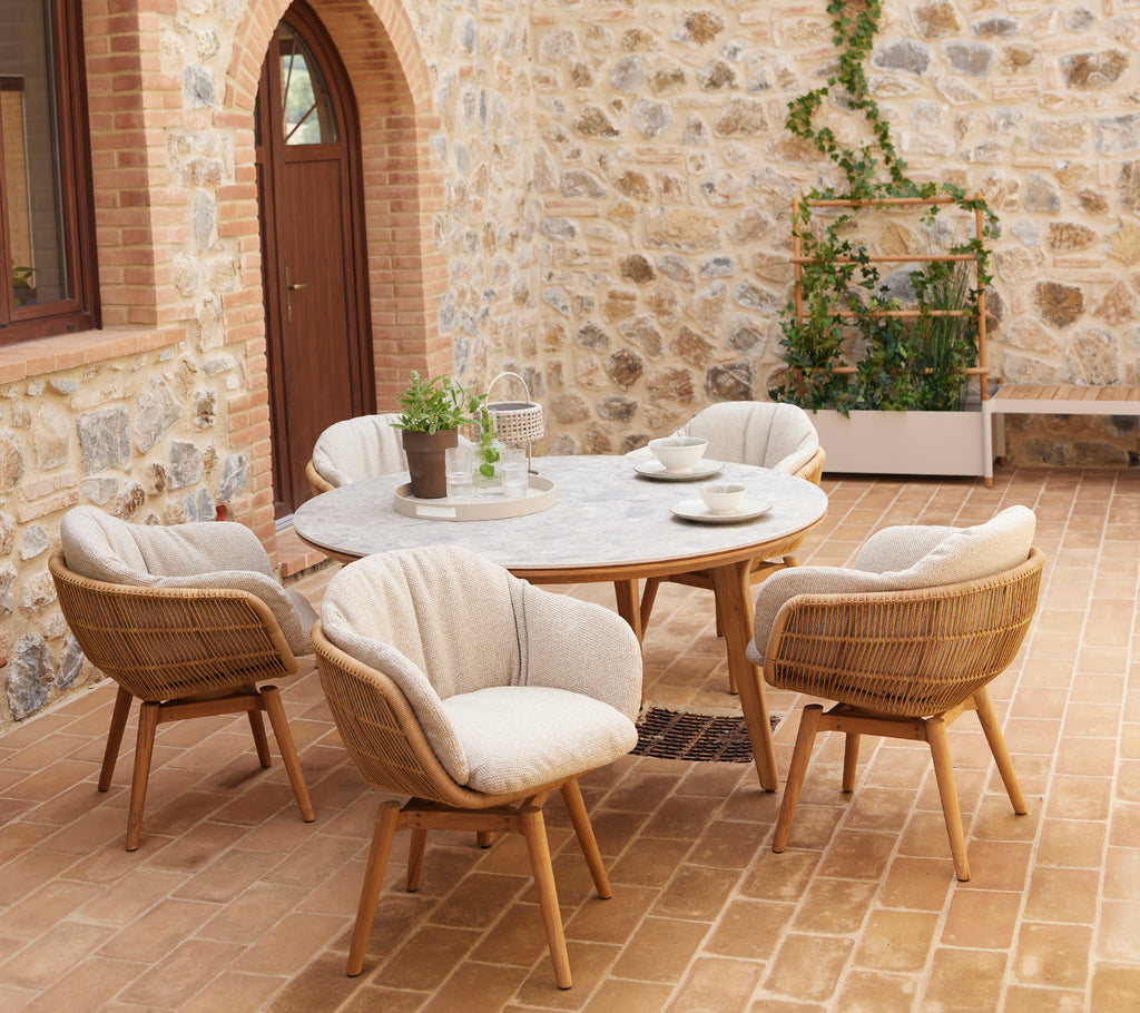 Una zona de estar elegante con sillas redondeadas y una mesa circular, complementada con vegetación en una maceta contra una pared de piedra.