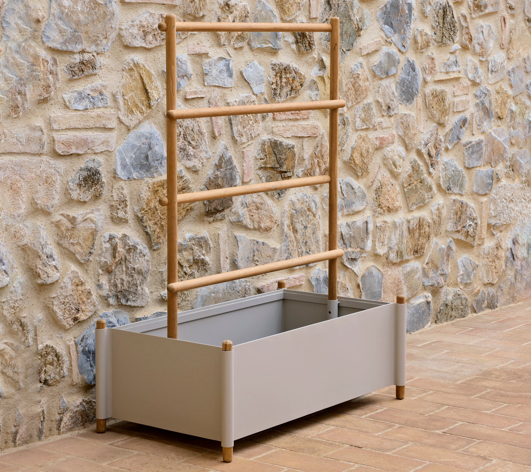 Una maceta de aluminio gris con un soporte de madera, diseñada para cultivar plantas, contra una pared de piedra texturizada.