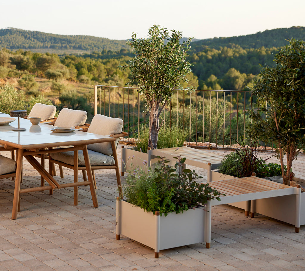 Una zona de estar elegante con una mesa, sillas cómodas y macetas llenas de vegetación, que realzan un paisaje sereno.