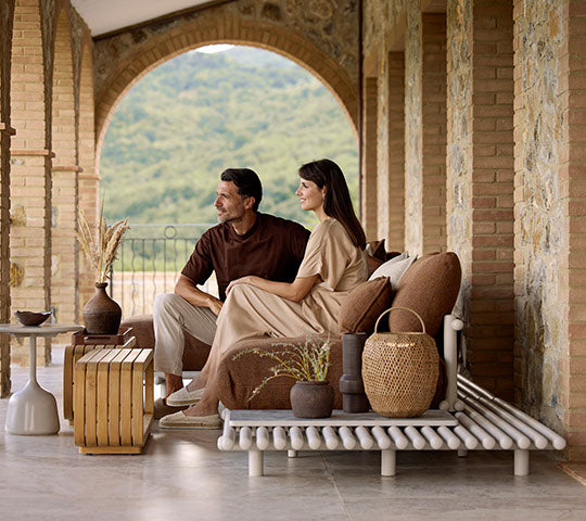 Una pareja se sienta junta en un sofá elegante, complementado por una mesa de café, jarrones decorativos y una lámpara colgante elegante.