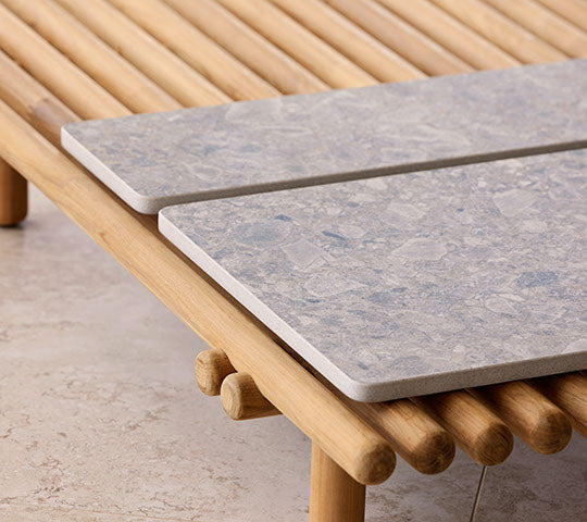 Una plataforma de madera cuenta con dos mesas de piedra, destacando un diseño moderno con elementos naturales para una exhibición elegante.