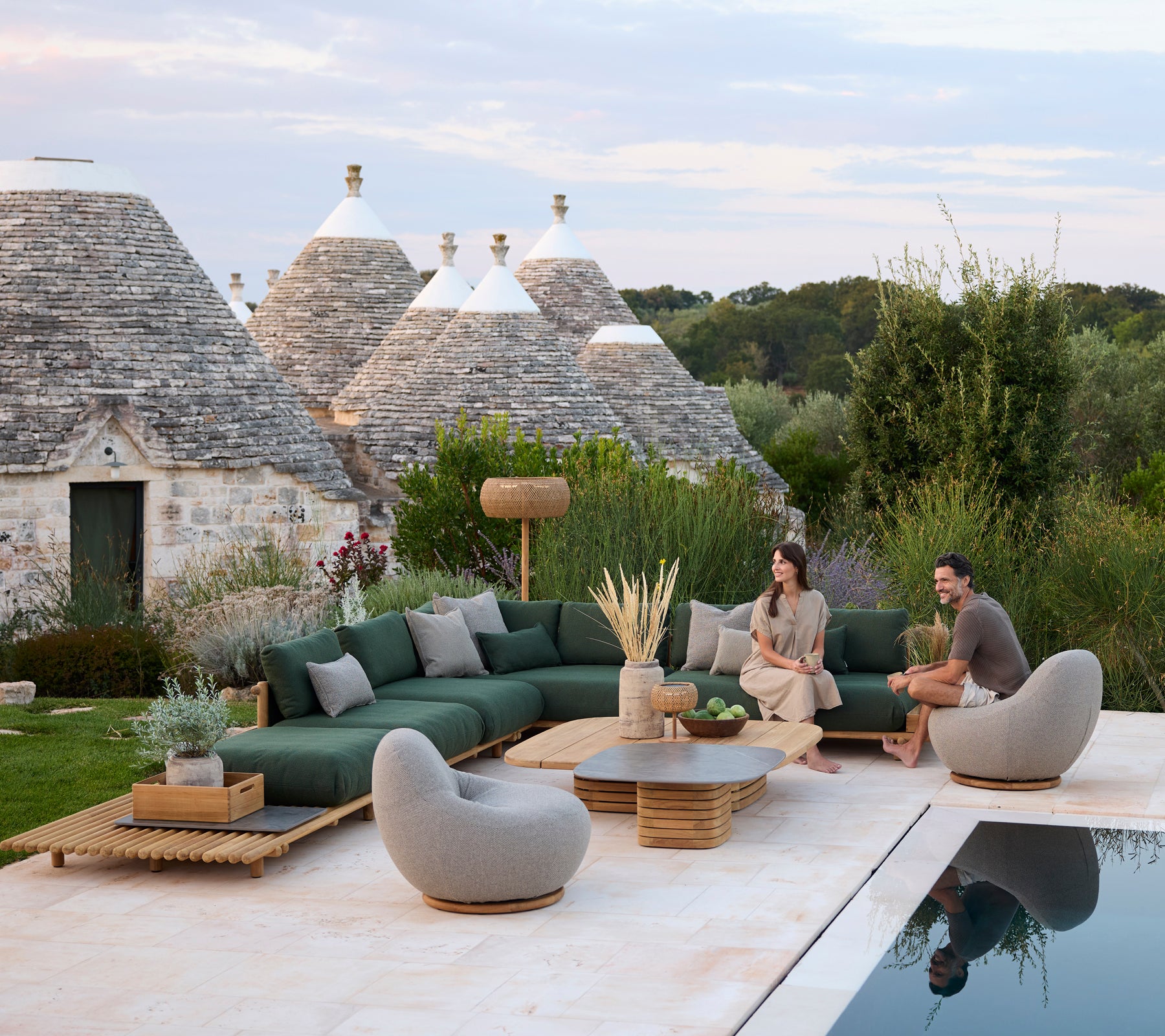 Zona de estar al aire libre moderna con sofá seccional verde y sillas grises junto a una piscina.