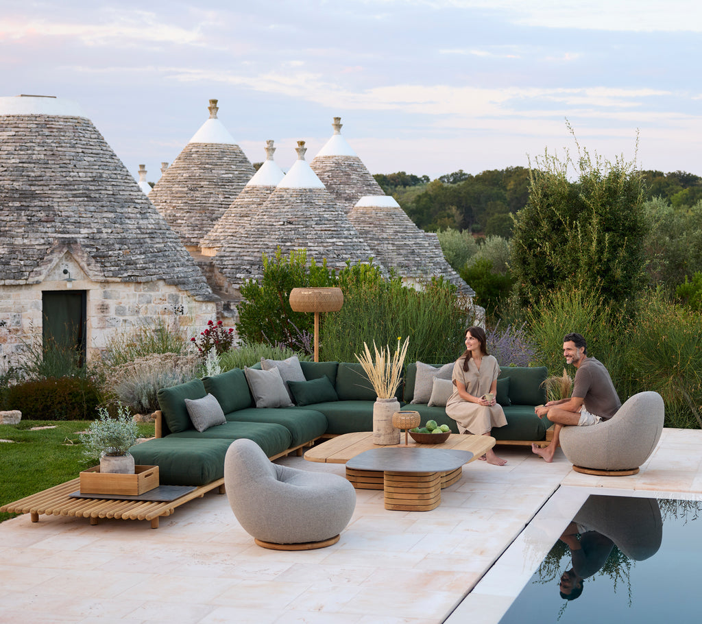Zona de estar al aire libre moderna con sofá seccional verde y sillas grises junto a una piscina.