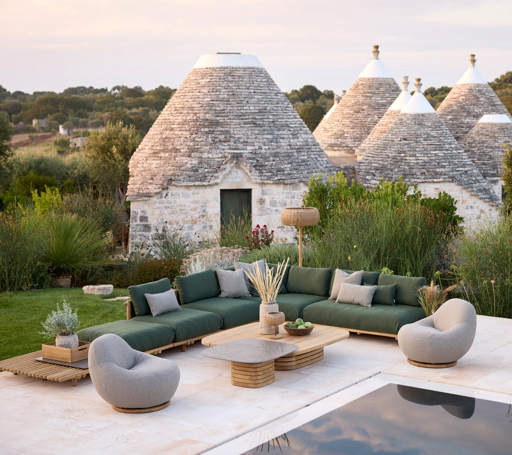 Moderna área de lounge exterior con sofá seccional verde, sillones grises y mesa de café de madera.