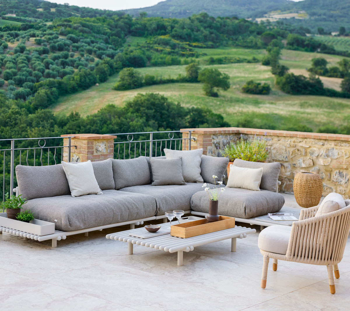 Área de lounge elegante con un sofá seccional gris y una silla cómoda, ubicada frente a un paisaje escénico.