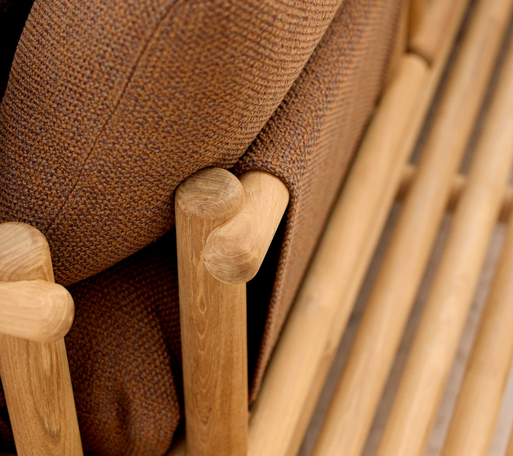 Sillón lounge de teca con cojines suaves y elegantes varillas de madera que forman el reposabrazos y la estructura base.