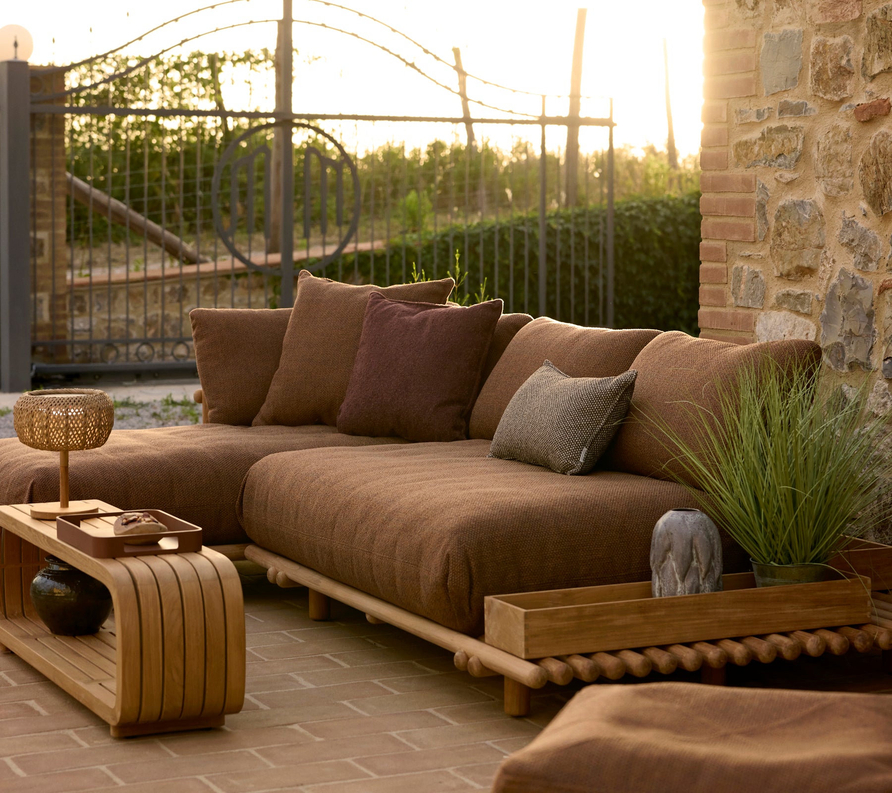 Mesa de café tranquila y caja de almacenamiento de teca junto a un acogedor área de estar al aire libre con cojines y plantas a la luz cálida de la tarde.