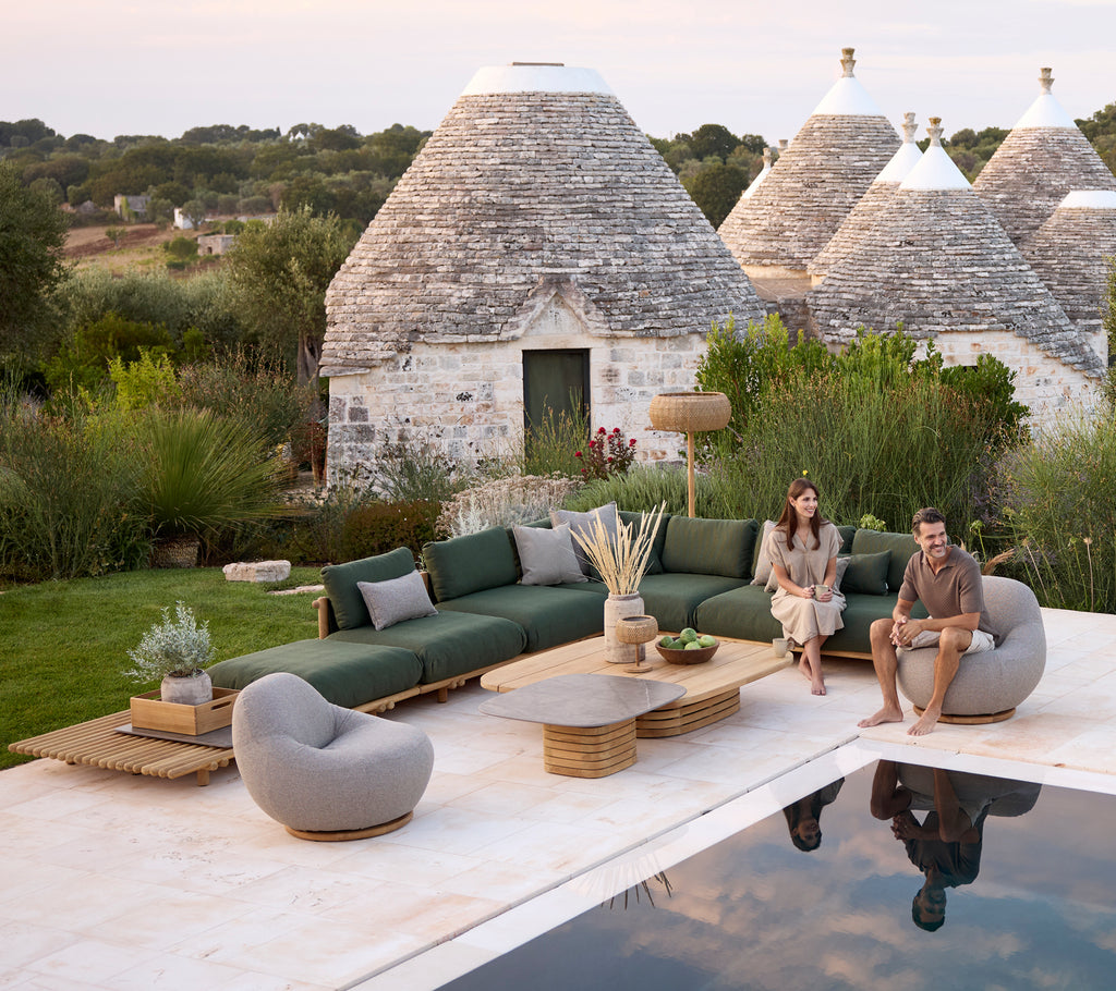 Moderna zona de lounge al aire libre con un sofá verde, una silla gris y una mesa de café redonda.
