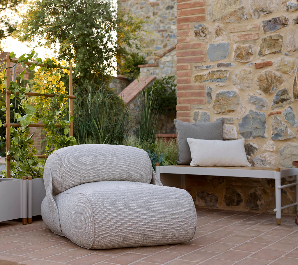 Una silla de lounge acogedora con una tela texturizada, acompañada de un banco de planta elegante y abundante vegetación en un entorno sereno.