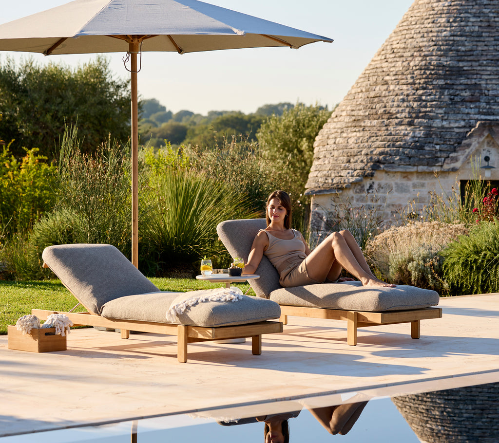 Dos tumbonas con cojines beiges bajo una sombrilla en un entorno exterior sereno.