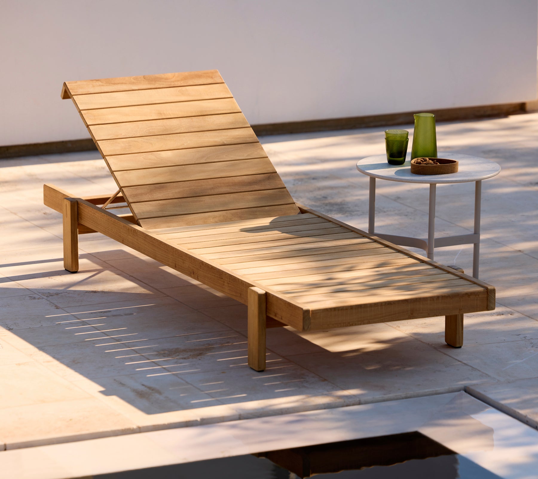 Tumbona de madera con una mesa auxiliar blanca en un entorno exterior moderno.