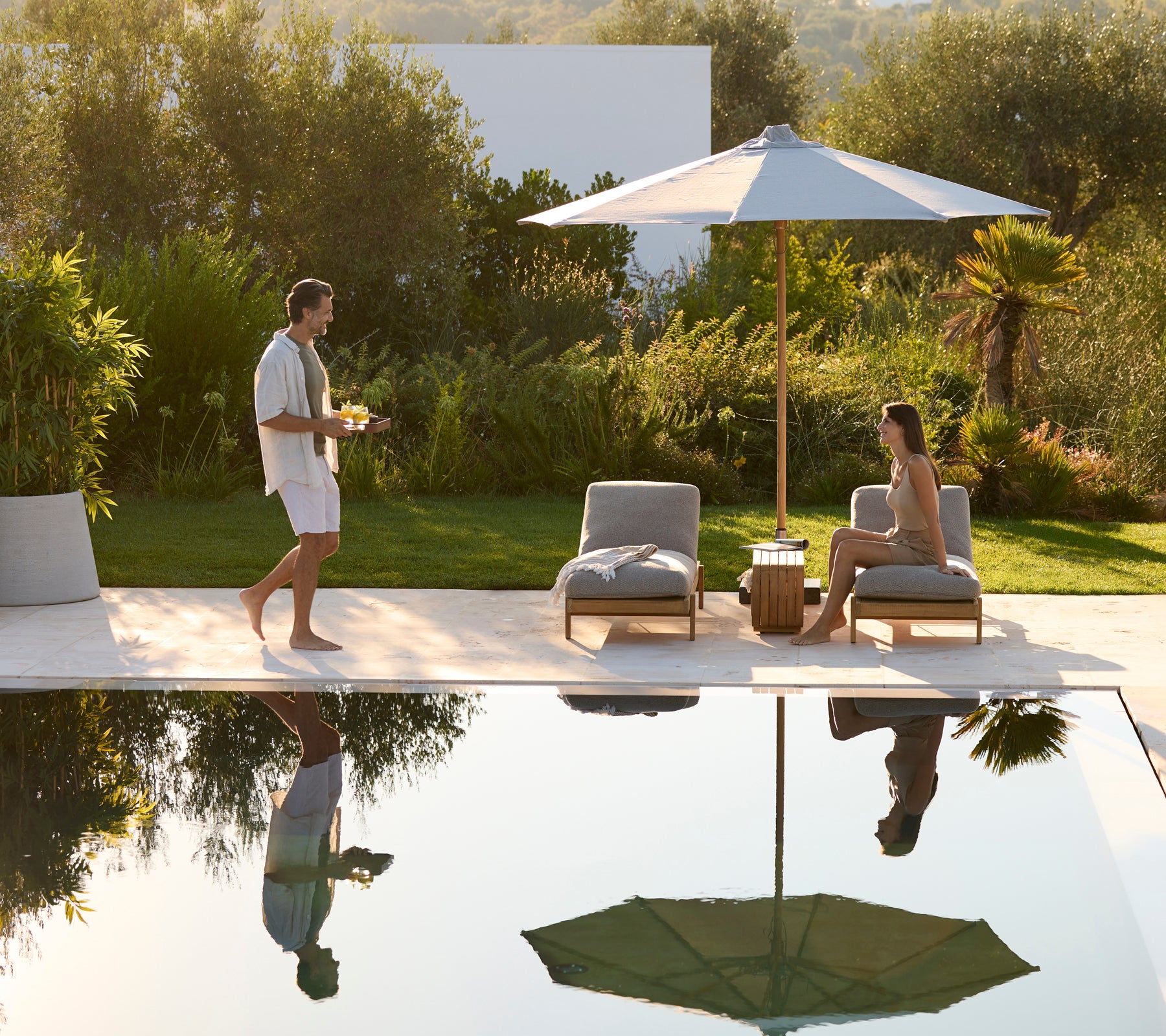 Área de salón moderna al aire libre con sillas grises, una mesa de madera y un paraguas verde.