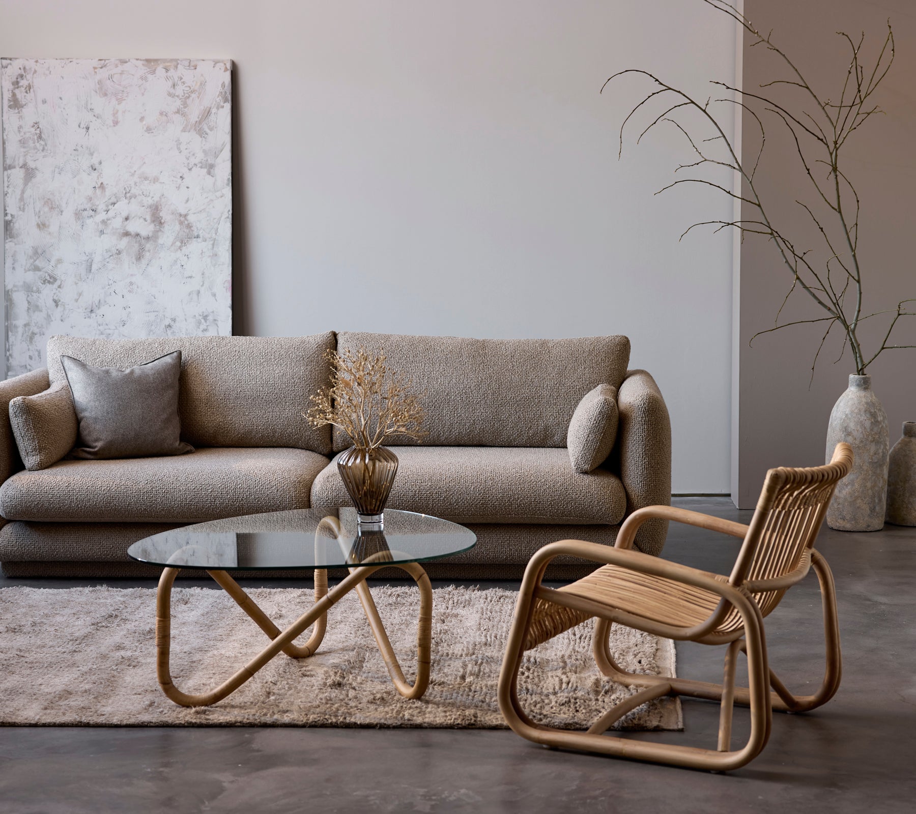 Configuración contemporánea de la sala de estar con un sofá beige, mesa de vidrio y silla de mimbre.