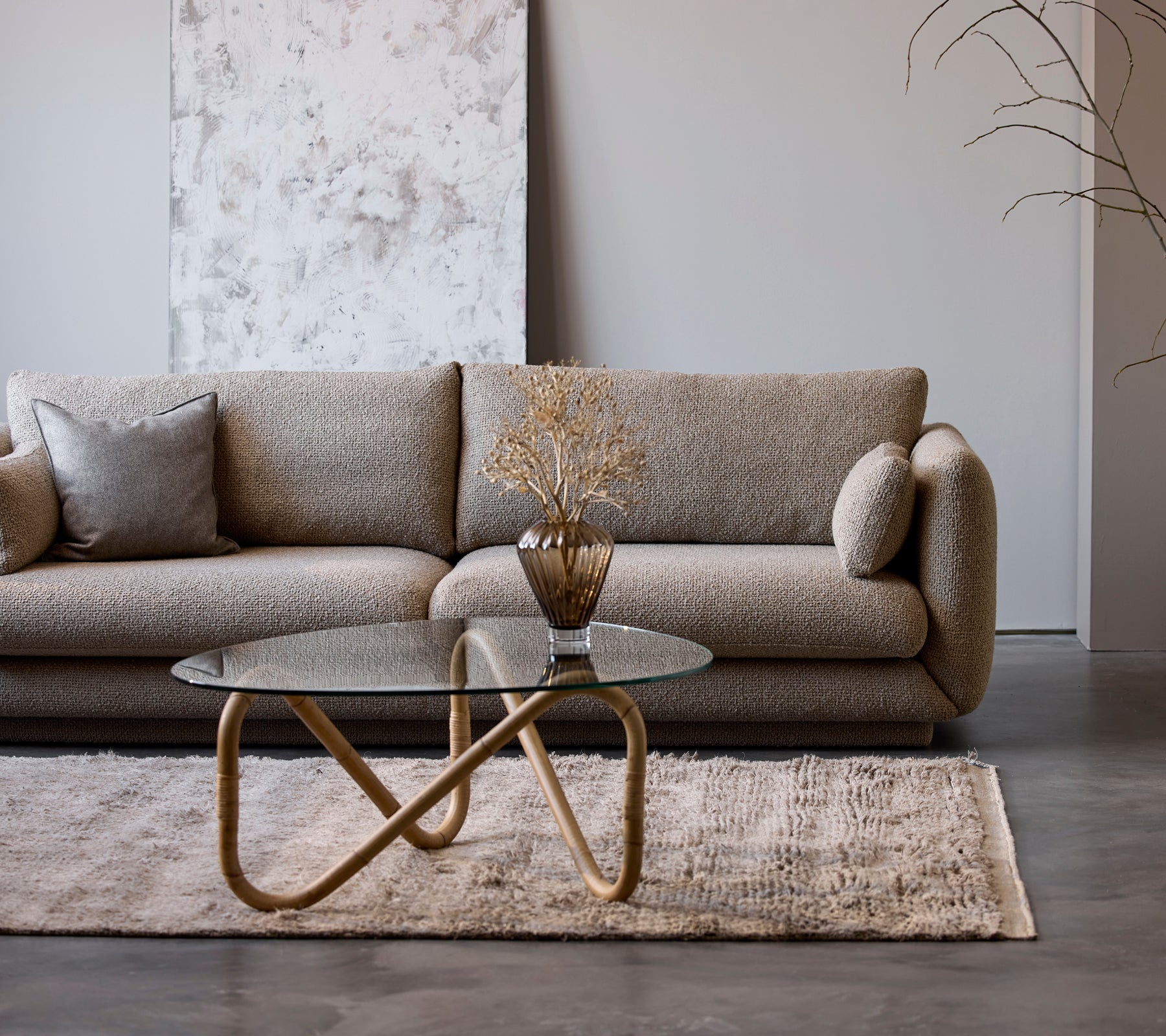 Un sofá beige moderno con una mesa de café de vidrio y un jarrón decorativo en un entorno de salón minimalista.