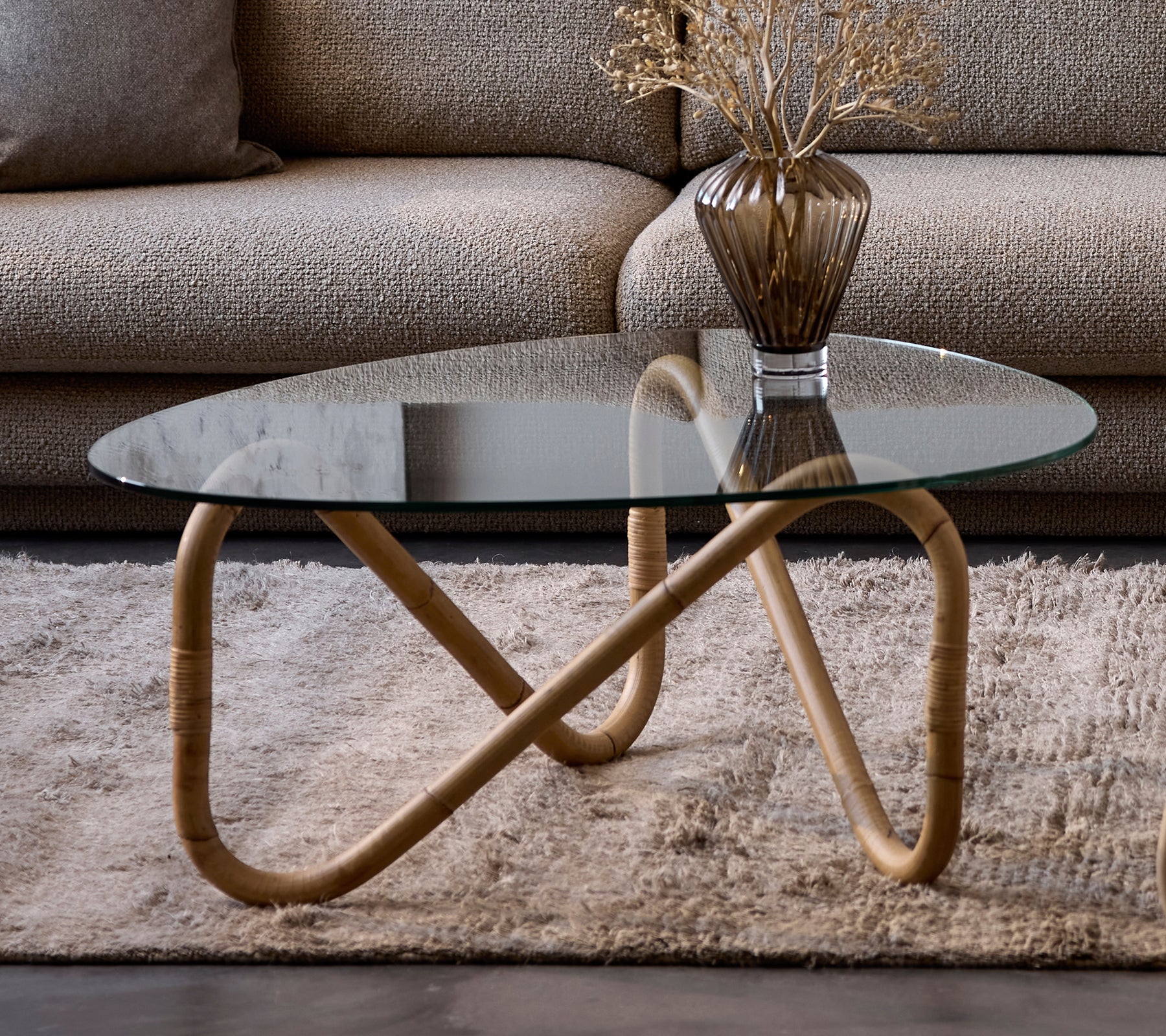 Mesa de café de vidrio moderna con un jarrón beige sobre una alfombra en un salón.