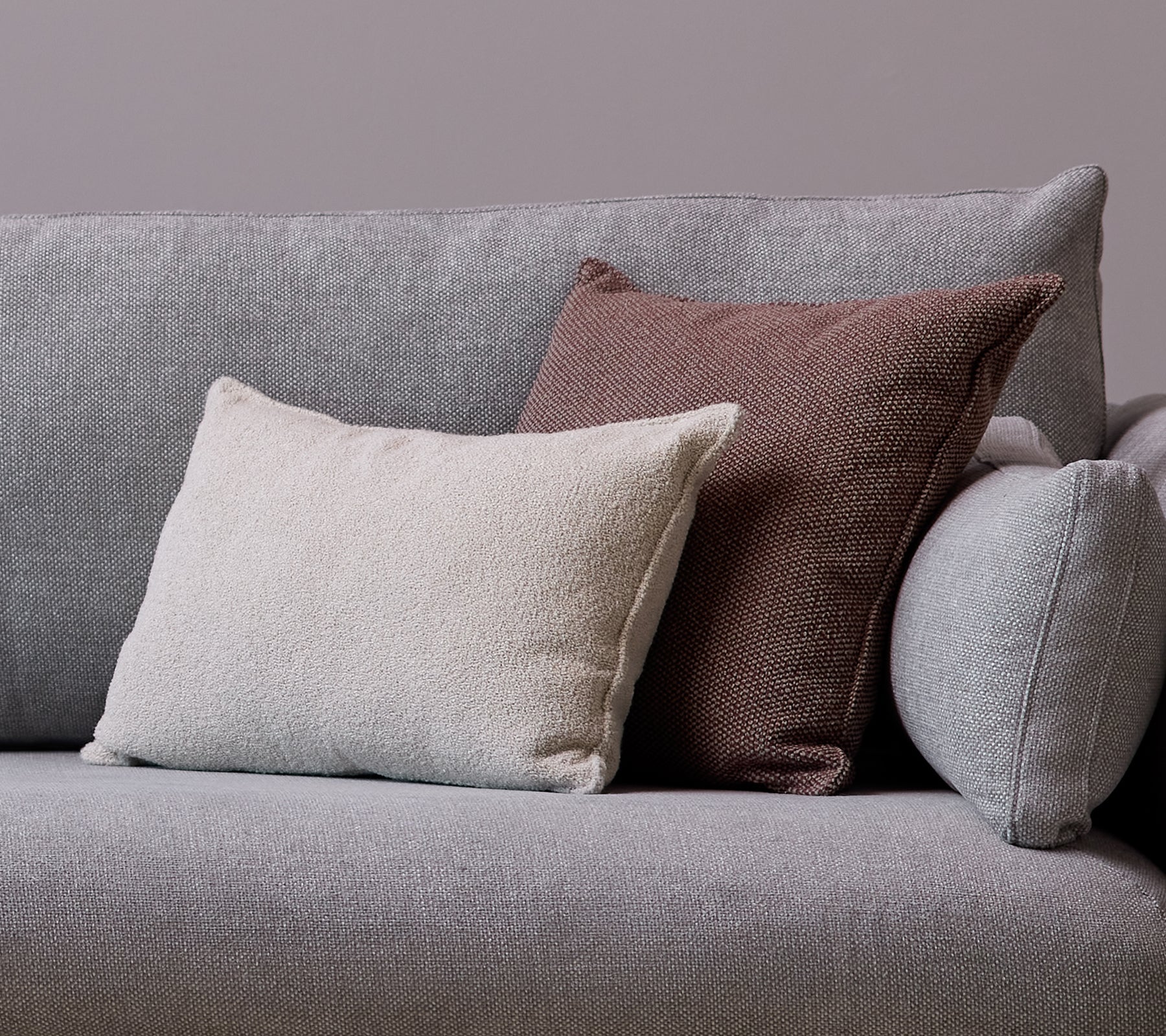 Una almohada scatter blanca Scent y una almohada Wove burdeos oscuro están colocadas en un sofá gris.