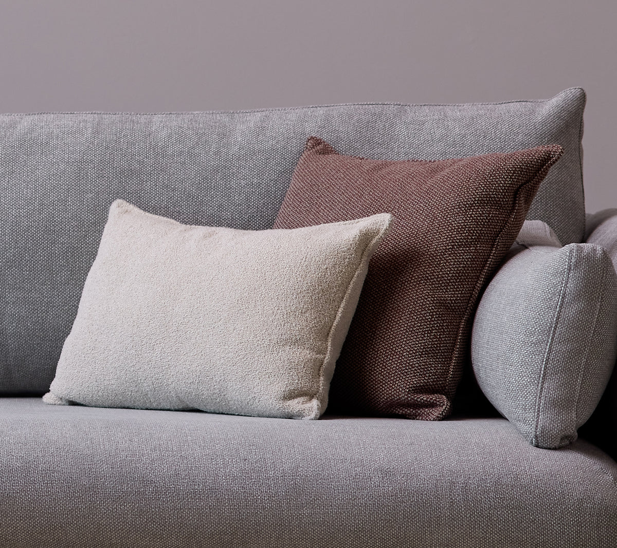 Una almohada scatter blanca Scent y una almohada Wove burdeos oscuro están colocadas en un sofá gris.
