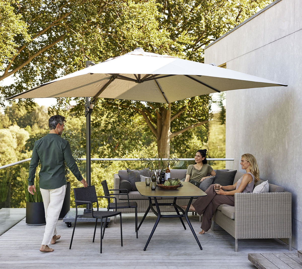 Una zona de estar elegante con una gran sombrilla, que cuenta con un sofá, sillas y una mesa de comedor rodeada de exuberante vegetación.