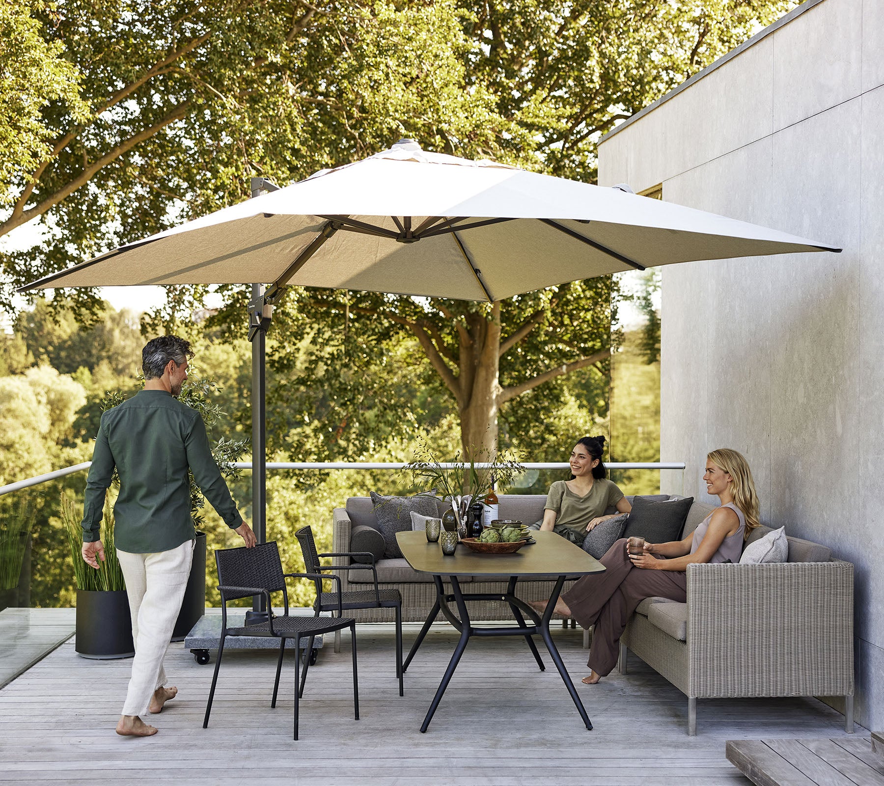 Una zona de estar elegante con una gran sombrilla, que cuenta con un sofá, sillas y una mesa de comedor rodeada de exuberante vegetación.