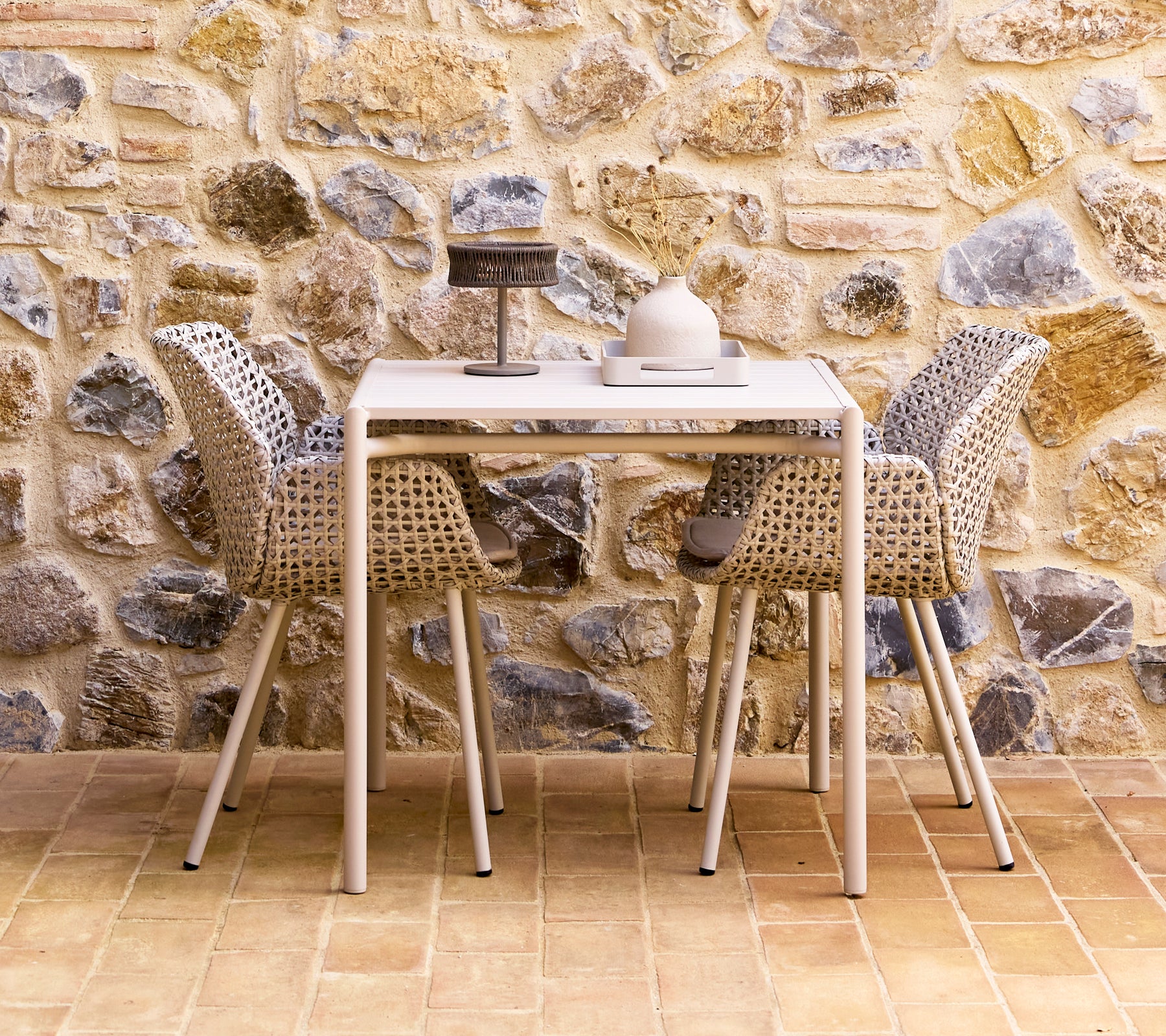 Un juego de comedor elegante con sillas de color arena dispuestas alrededor de una mesa moderna, contra una pared de piedra texturizada.